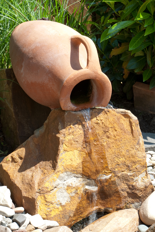 Water feature with an amphora and a bolder in an garden